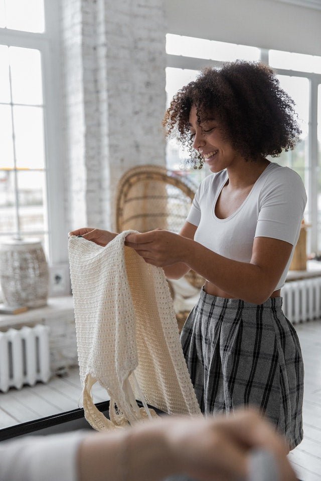 A biracial woman is smiling and holding a white knit dress.