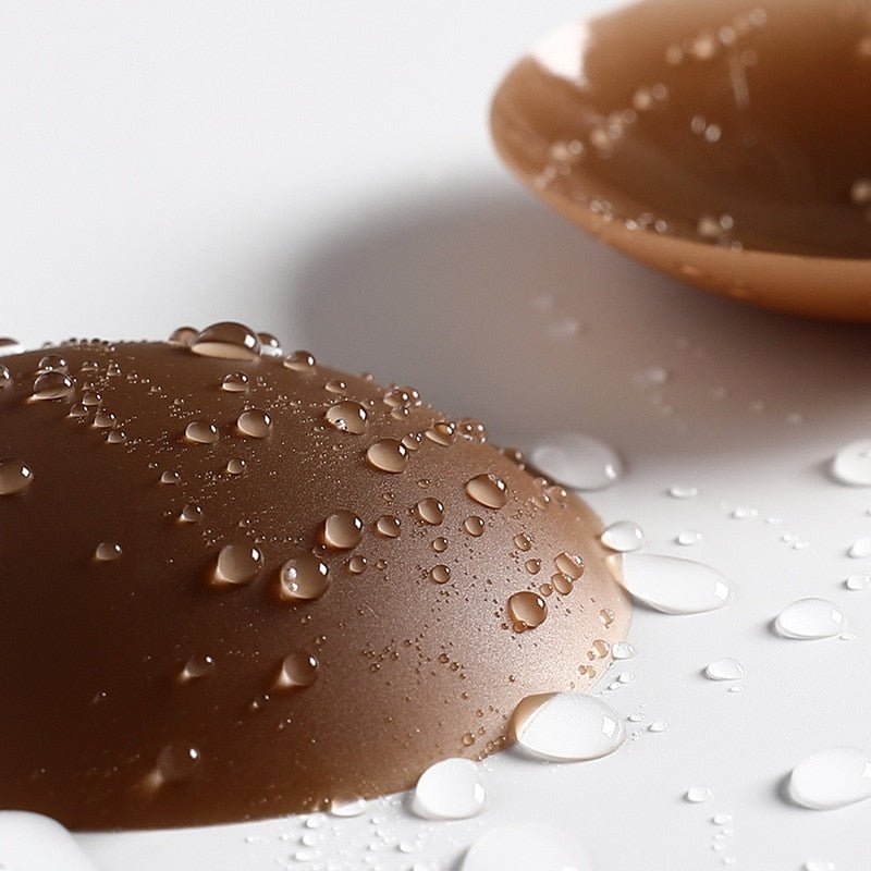 A pair of dark brown reusable nipple covered in drops of water.
