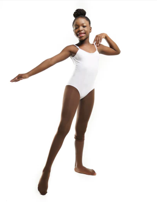 A photo of a happy young Black girl with dark skin posing in a white leotard and Blendz dark brown convertible dance tights in the color “confident cocoa” showing the tights over one foot and up her leg.