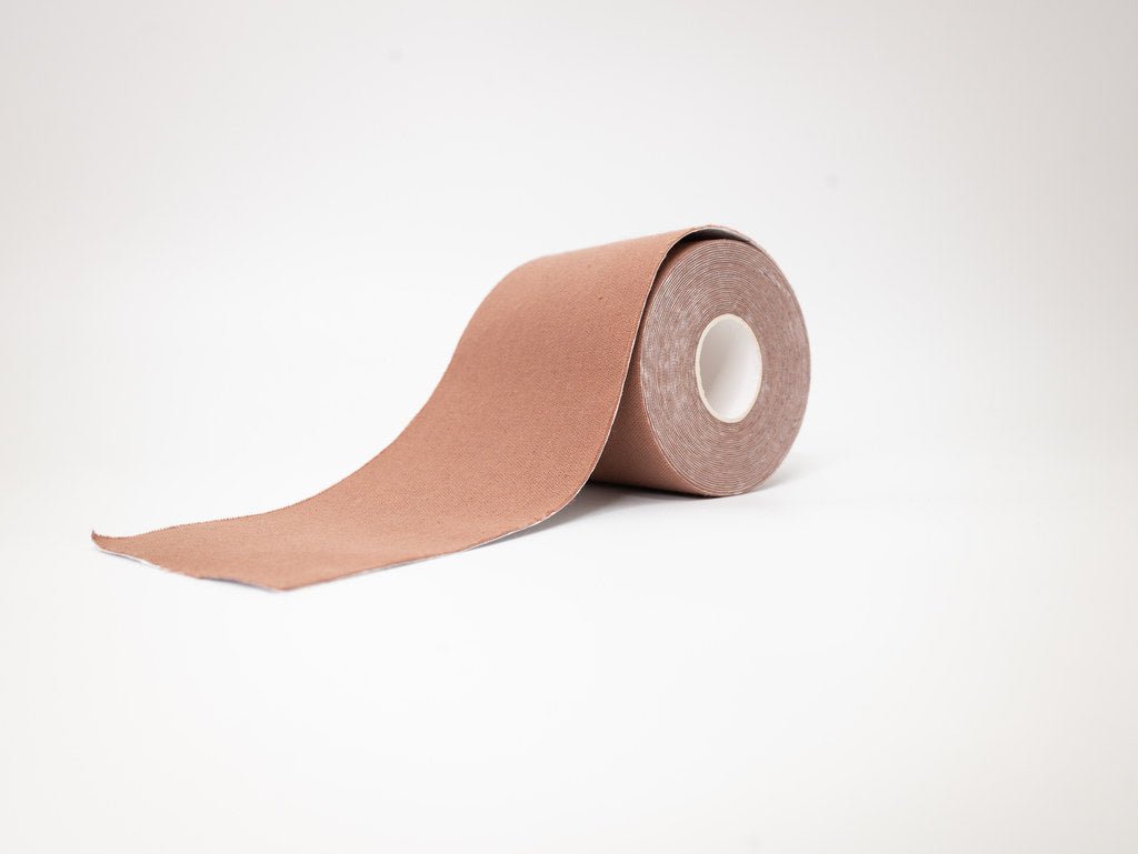 A roll of light brown boob tape for a strapless bra on tanned to medium brown skin.