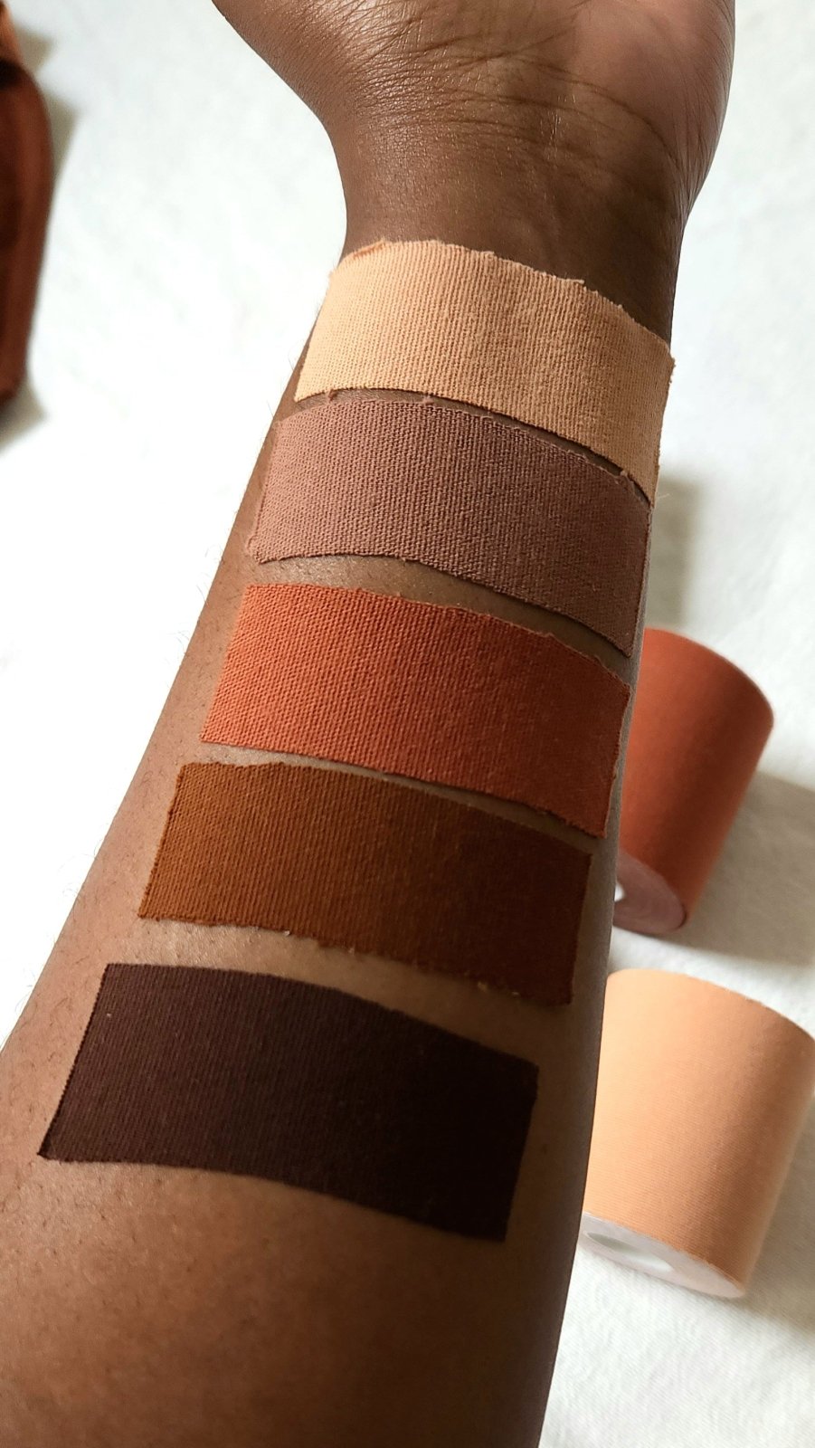 Boob tape swatches on a dark brown woman's skin.